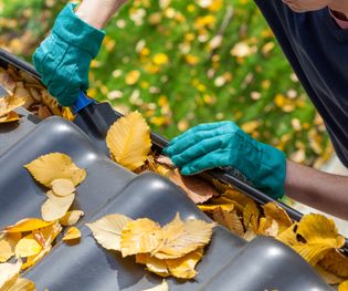 Man cleaning the gutter from autumn leaves
